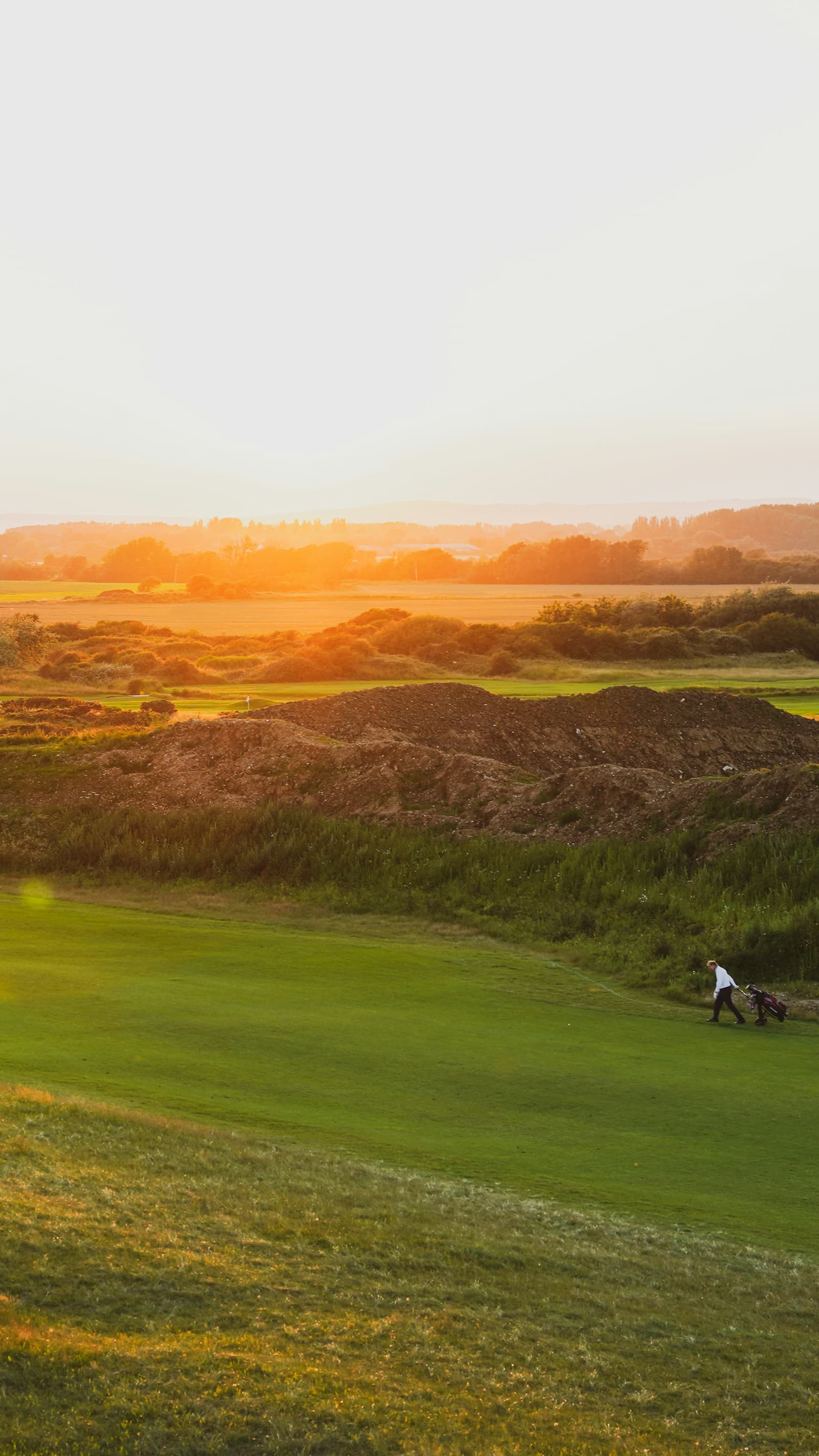 A golfer walking a links fairway in the evening light